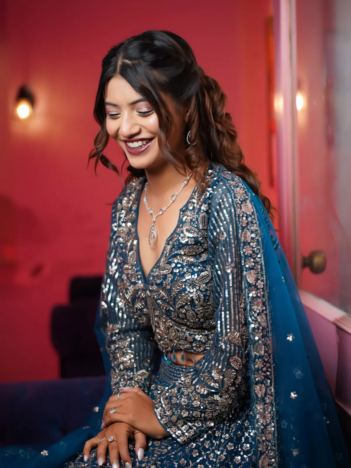 A model in a teal sequin lehenga laughing, with rose-gold eye makeup by Nitya
