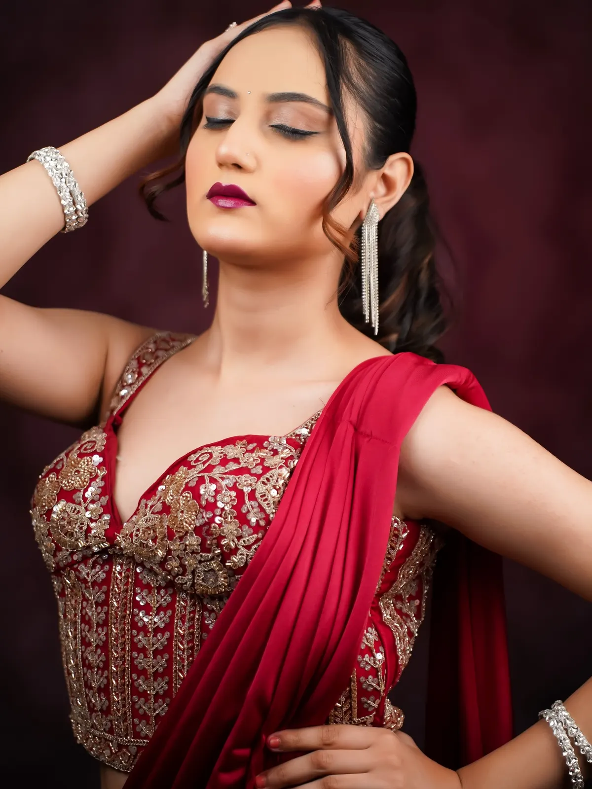 Model in a red drape saree with eyes closed and berry lips