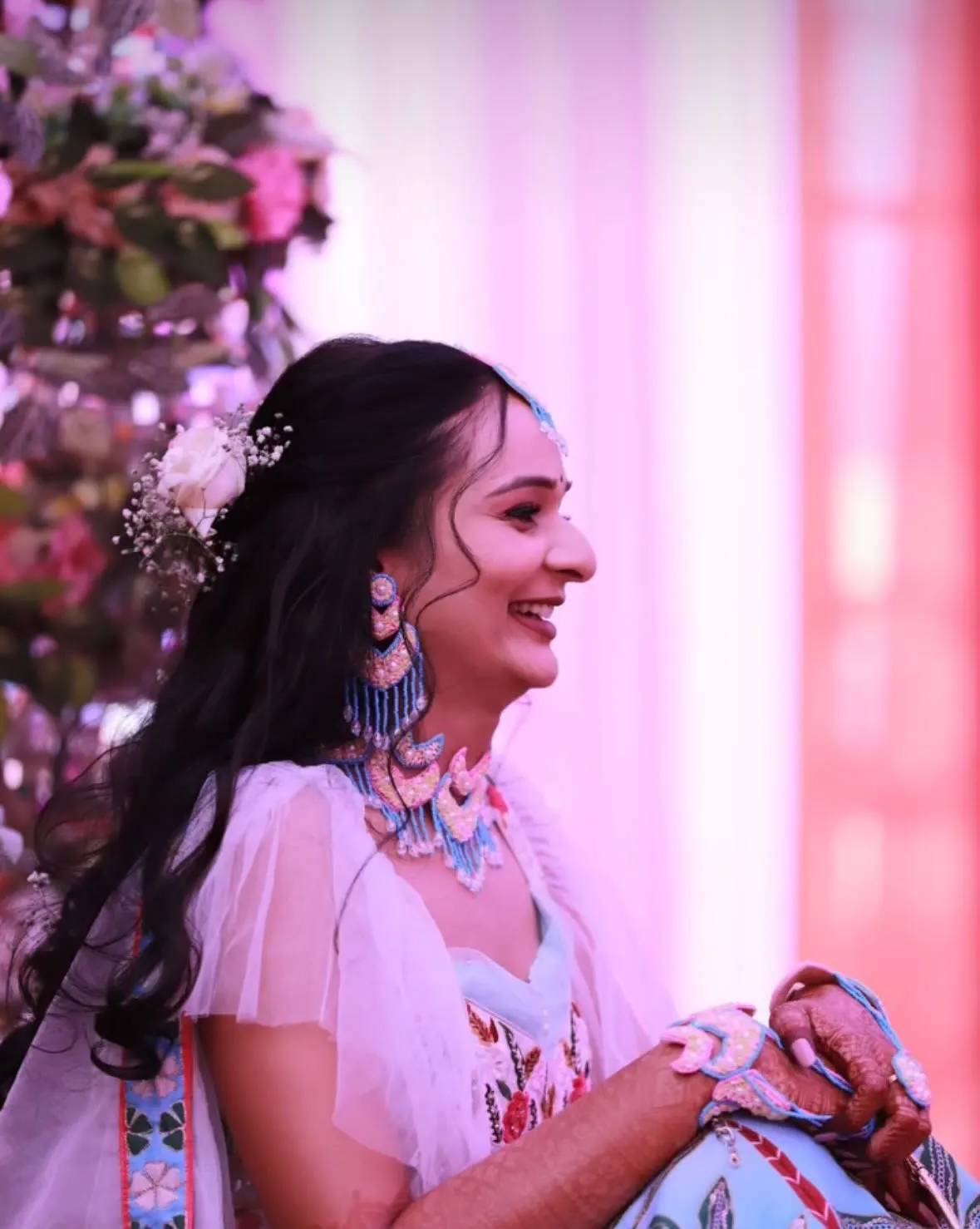 Bride laughing in profile at her haldi, pastel floral earrings